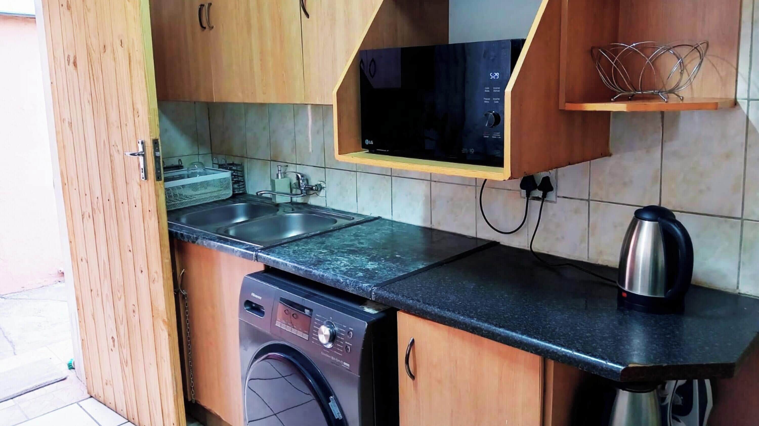 A compact kitchen with a dishwasher, a microwave, and a kettle.