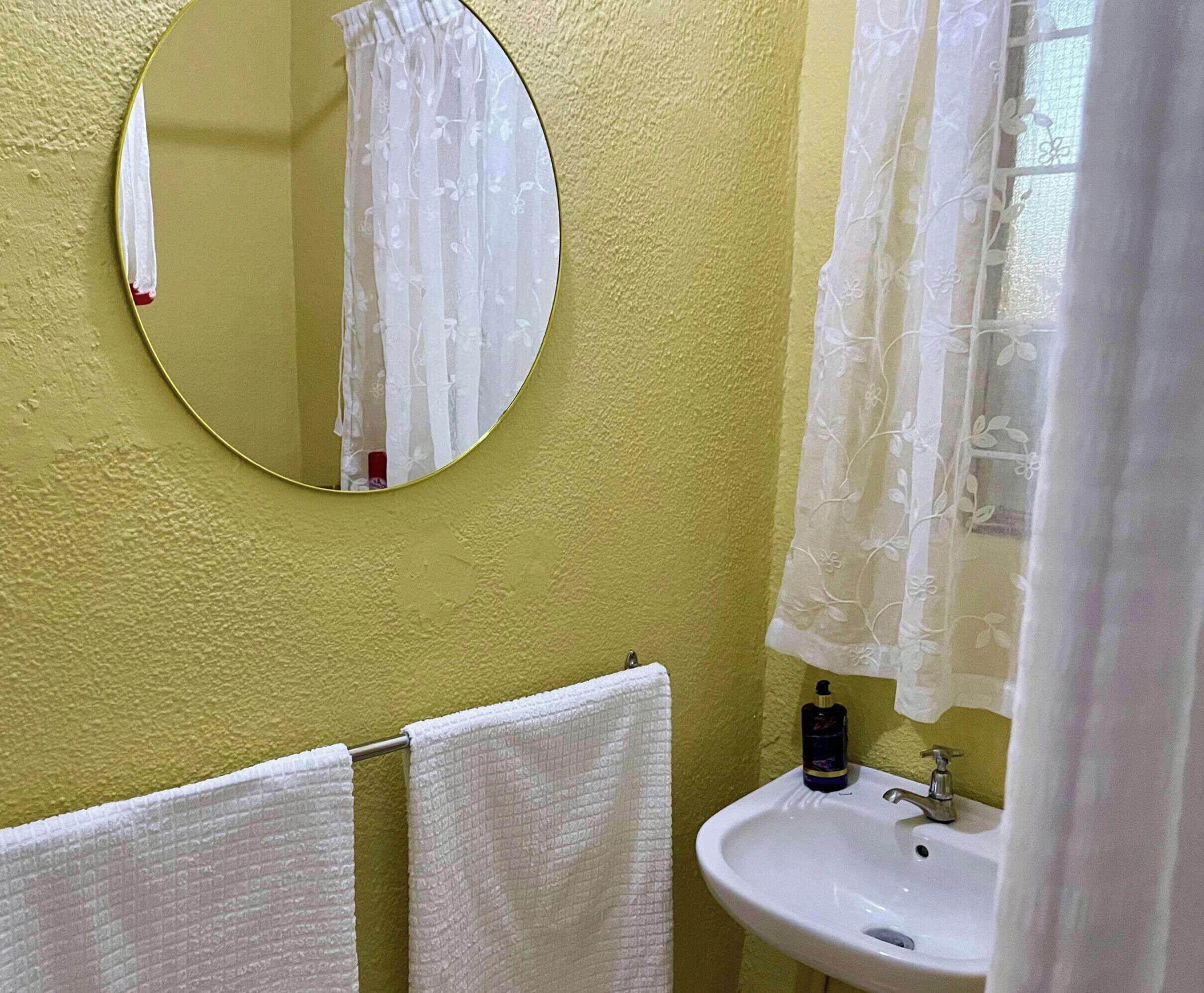 Un baño con un espejo redondo, un lavamanos y un perchero para toallas.