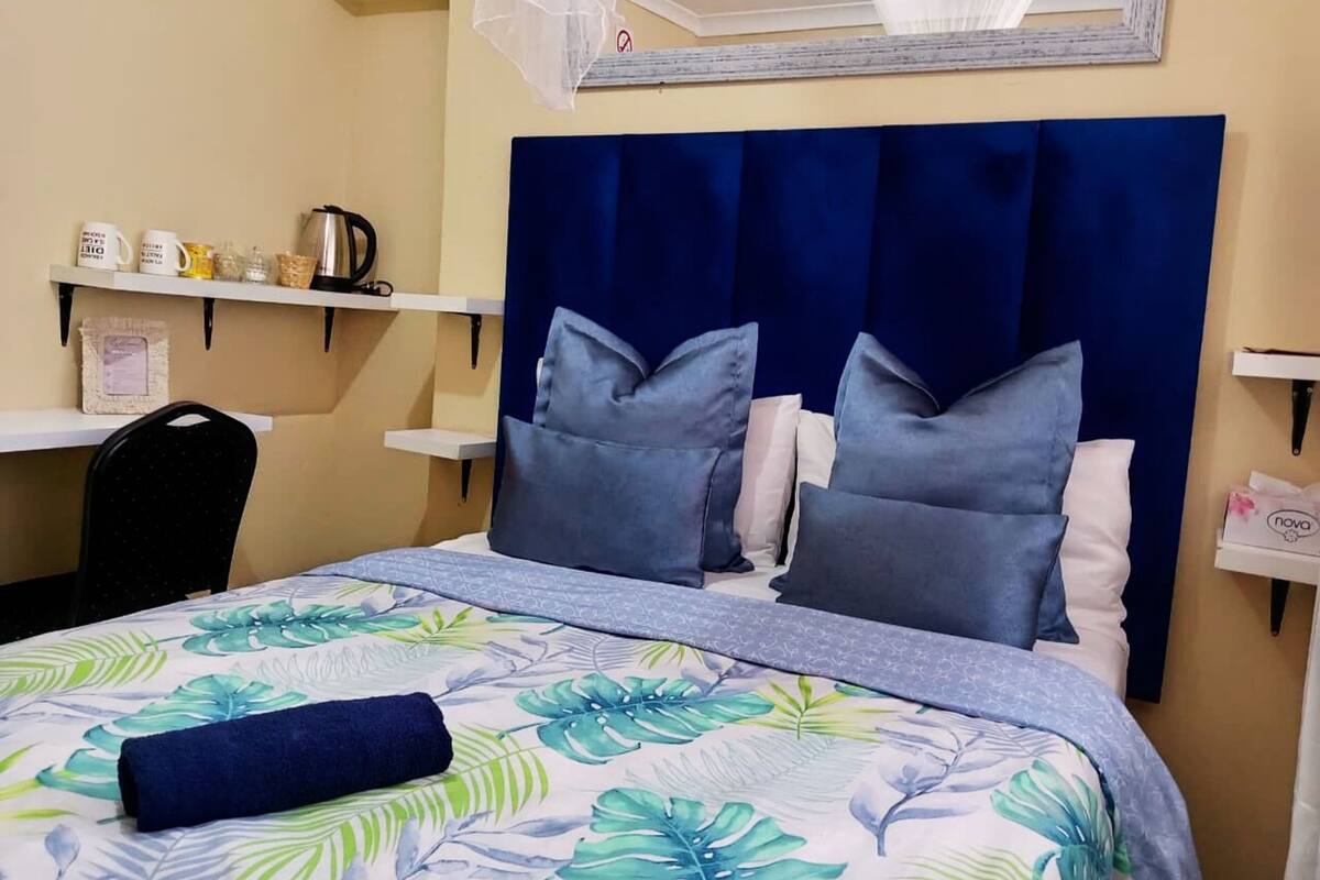 Un lit bien fait, recouvert d’une couvre-lit à motifs floraux, avec deux oreillers et une tête de lit bleue.