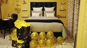 A hotel room with a bed, bedside tables, a nightstand, and a dining area with a table set for two. - Budget Stays At Olivia Pines Guesthouse  (Krugersdorp)