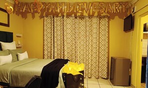 A hotel room with a bed, a television, a curtain, and a gift bag. - Budget Stays At Olivia Pines Guesthouse  (Krugersdorp)