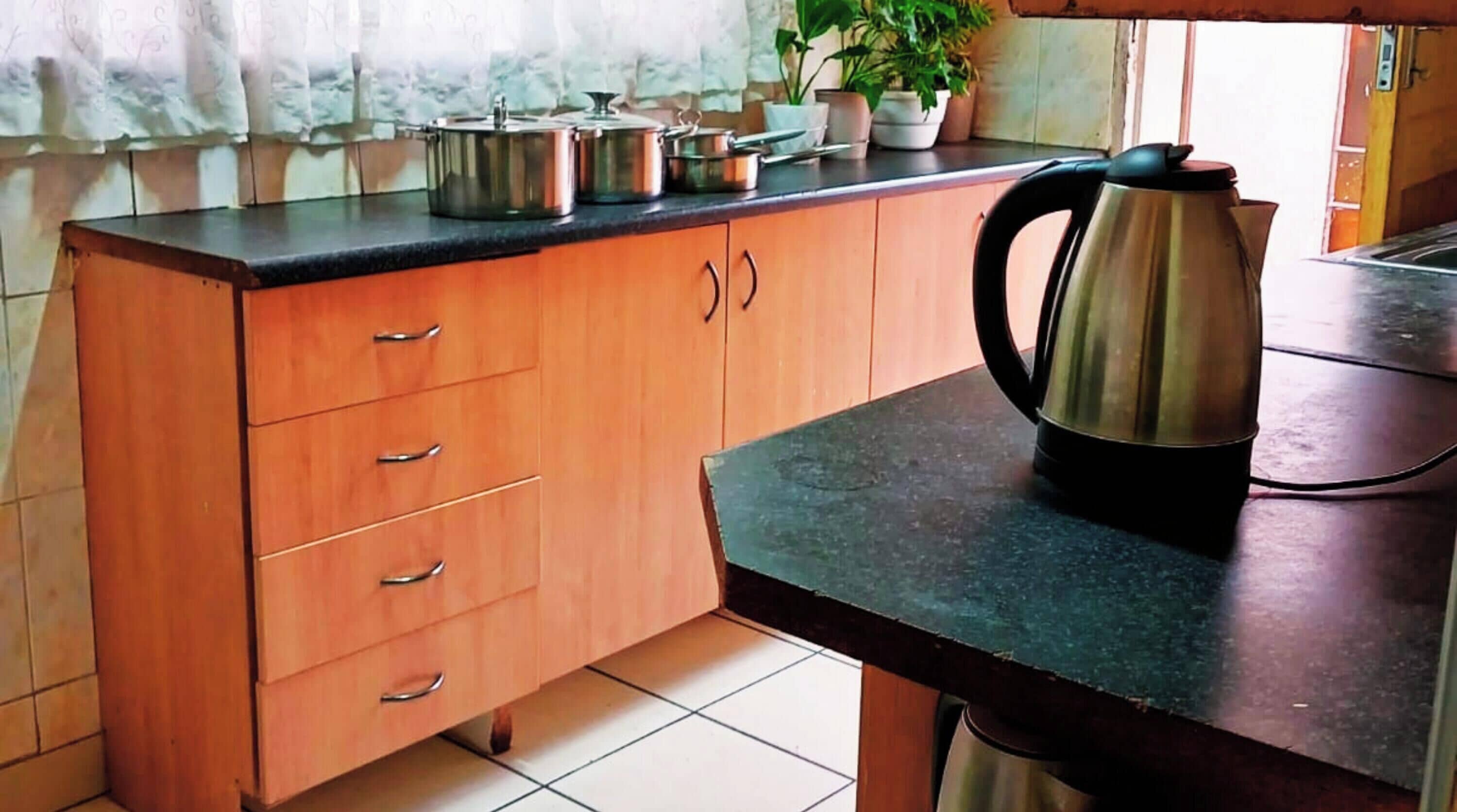 A kitchen with a wooden cabinet, a countertop, and a kettle.