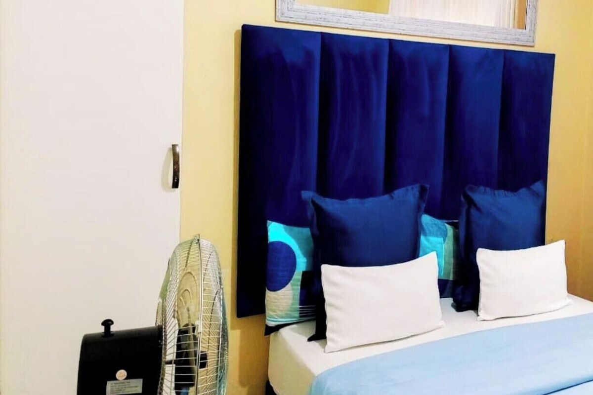A hotel room with a bed, a fan, and a window with curtains.