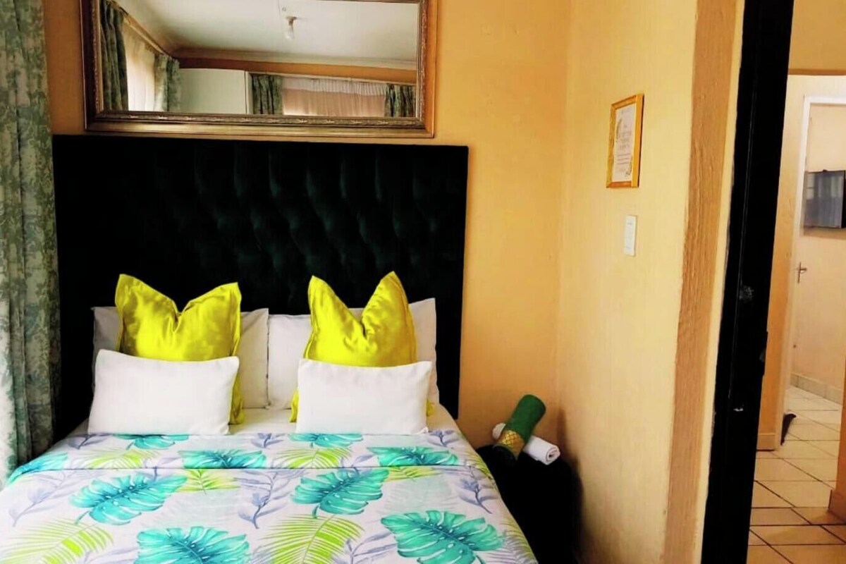 A hotel room with a bed, two pillows, a headboard, a door, and a wall with a framed picture.