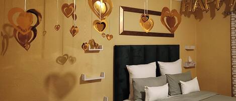 A bedroom with a bed, pillows, a headboard, and heart-shaped decorations on the wall.