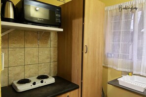 A kitchen with a microwave, stove, and wooden cabinets. - Budget Stays At Olivia Pines Guesthouse  (Krugersdorp)