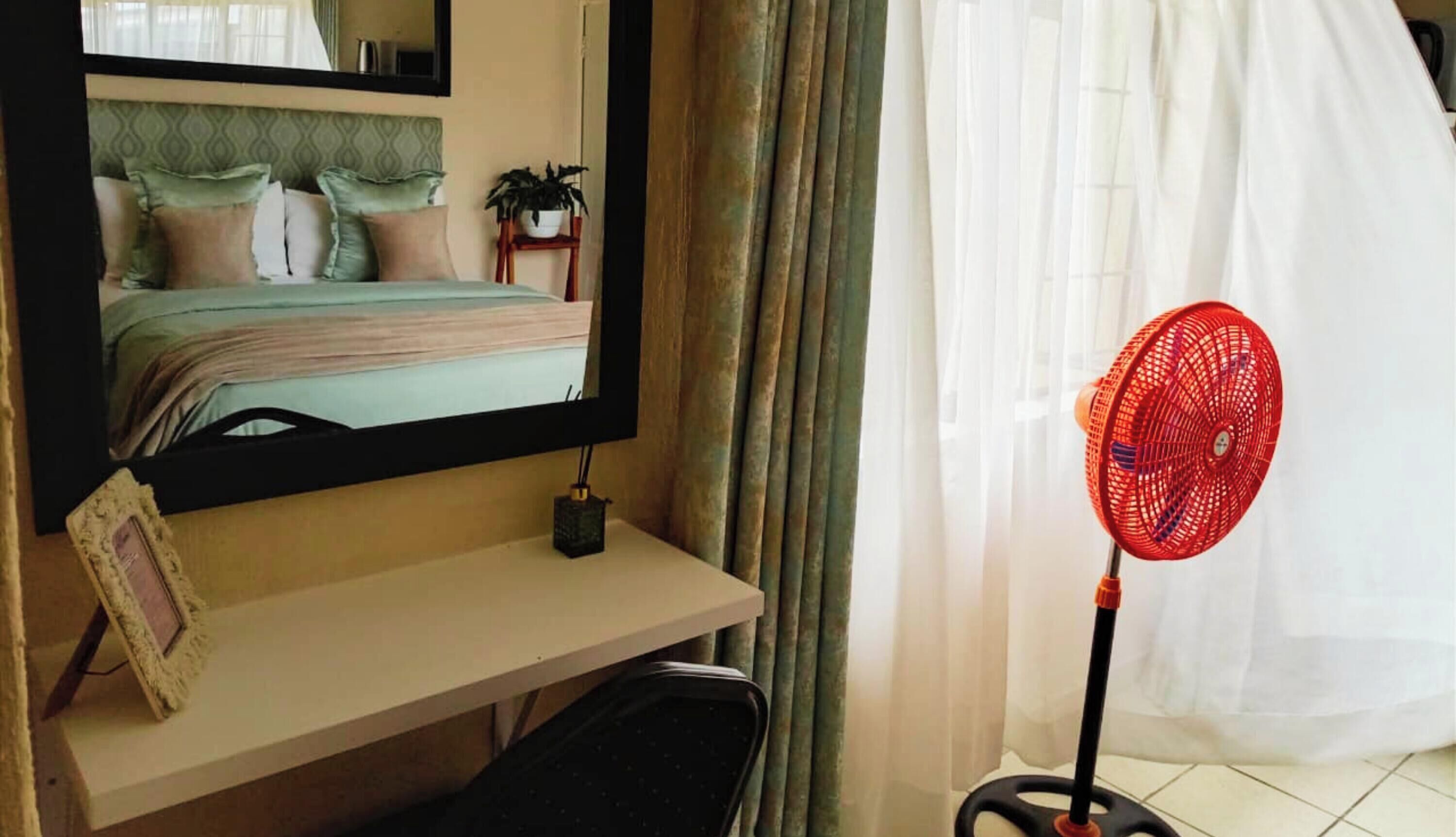 A hotel room with a bed, a desk, a chair, a red fan, and a window with curtains.