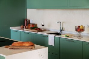 A kitchen with green cabinets, a marble countertop, a loaf of bread, a wine glass, and a fruit bowl. - Villa Rossa - by My Home in Como (Brunate)