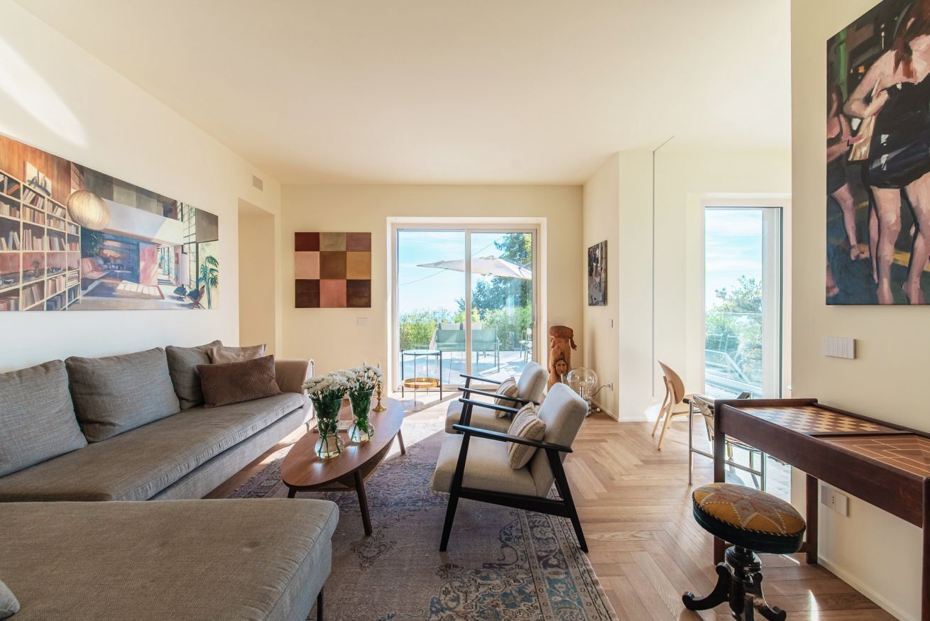 Ein modernes Wohnzimmer mit einer Couch, einem Sessel, einem Couchtisch und einem Klavier. Ein großes Fenster bietet Blick ins Freie.