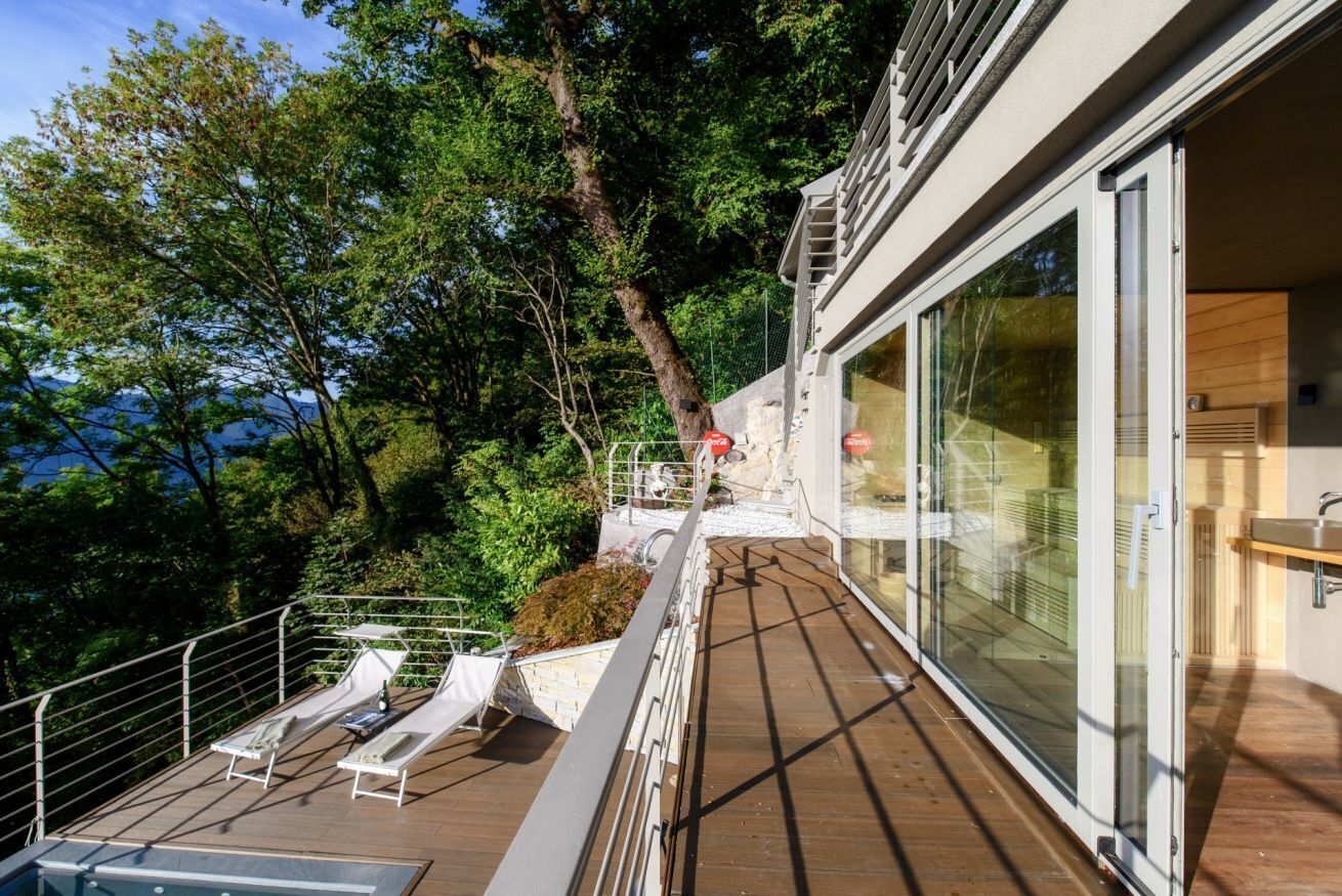 A modern outdoor deck with lounge chairs, a pool, and a glass-enclosed room.