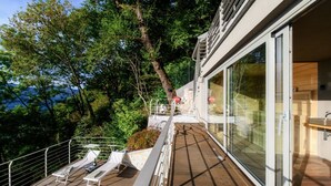 A modern outdoor deck with lounge chairs, a pool, and a glass-enclosed room.