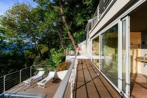 A modern outdoor deck with lounge chairs, a pool, and a glass-enclosed room.