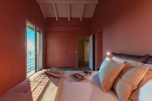 Una camera da letto con un letto, cuscini, un vassoio con degli oggetti, una finestra e una porta che conduce a un'altra stanza.