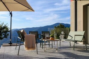 An outdoor seating area with chairs and tables, a large umbrella, and a scenic mountain view.