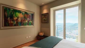 A bedroom with a large window, a bed, a painting, and a small table.
