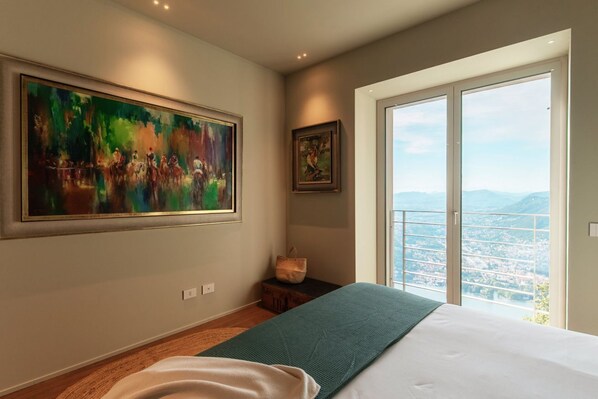 A bedroom with a large window, a bed, a painting, and a small table.