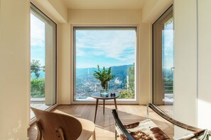 A room with a large window, a round table with a vase, a chair, and a sofa. - Villa Rossa - by My Home in Como (Brunate)