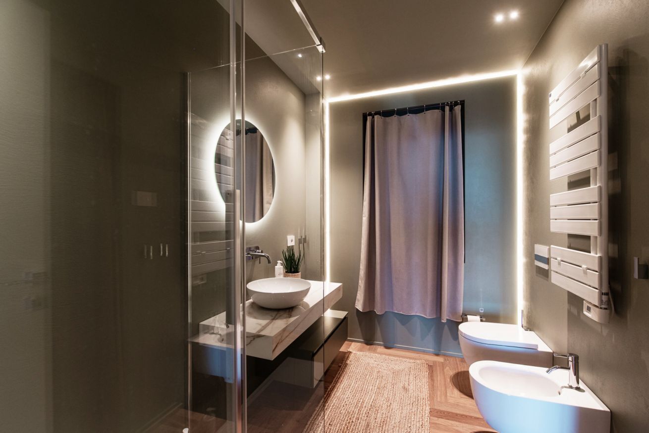 A modern bathroom with a glass shower enclosure, a round mirror, a freestanding sink, and a toilet.