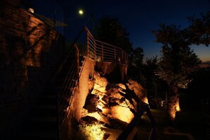 A stone staircase leading up to a metal railing, surrounded by trees and a street lamp.