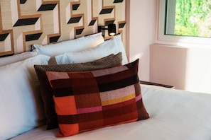 Un letto con lenzuola bianche, una testiera a motivi geometrici e una finestra vista verde.