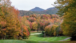 Un parcours de golf avec un étang, entouré d’arbres aux couleurs automnales et avec une montagne en arrière-plan.