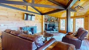 L’intérieur d’un chalet chaleureux, avec une cheminée en pierre, des meubles en cuir et des murs en bois.