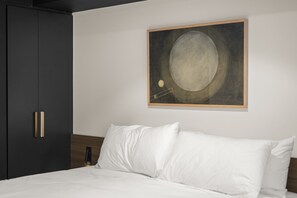 A bedroom with a bed, white pillows, a dark wardrobe, and a framed artwork on the wall. - Braddon Studio: Parking & BBQ (Canberra)