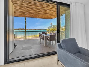 Een balkon met een tafel, stoelen, een grijze bank en uitzicht op zee.