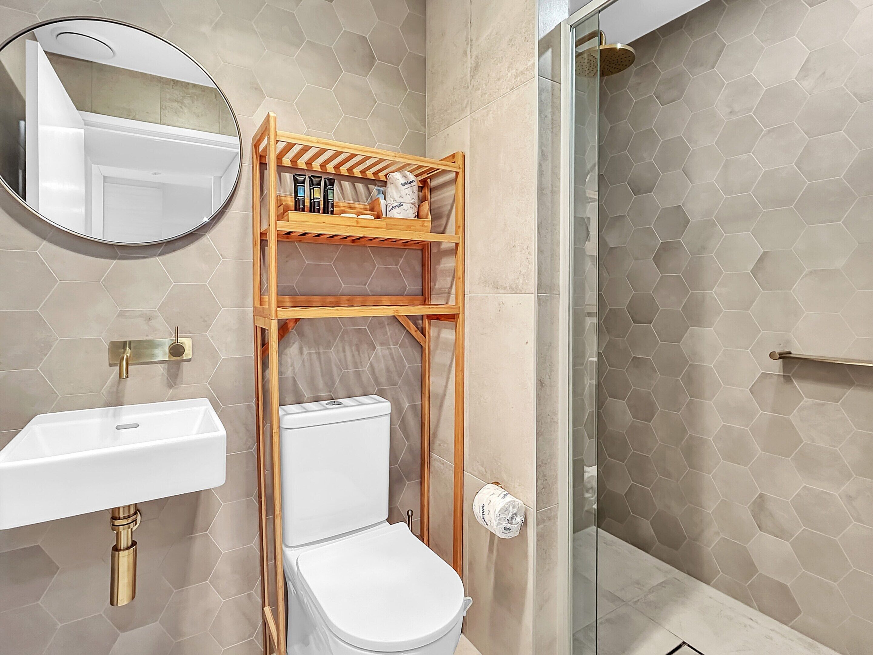Et moderne badeværelse med et hexagonalt flisemønster, en hvid vask, et toilet og en glasbrusekabine.