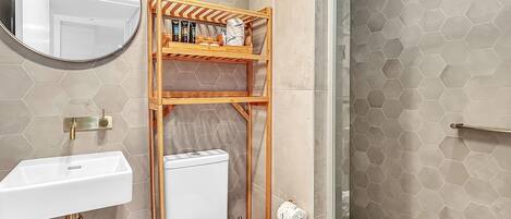 Et moderne badeværelse med et hexagonalt flisemønster, en hvid vask, et toilet og en glasbrusekabine.