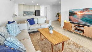 A modern living room with a sofa, coffee table, and a TV on a wooden stand. - 3-bed: Riverfront Alfresco Dining & Rooftop Pool (Batemans Bay)