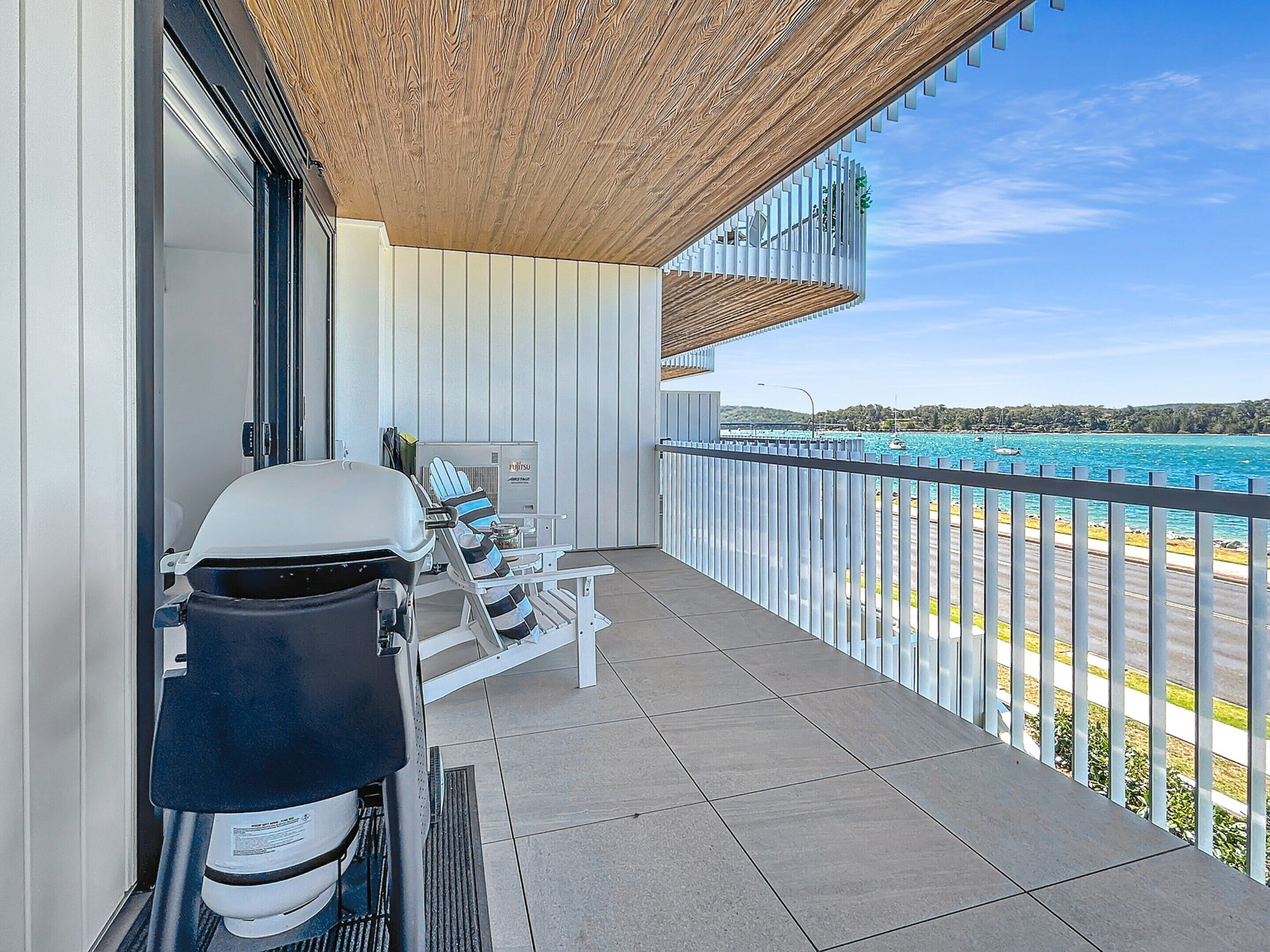A balcony with a grill, a chair, and a view of the sea.