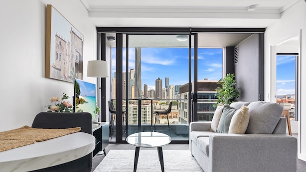 Un salon moderne avec un canapé, une table ronde et une vue sur le paysage urbain, visible à travers de grandes fenêtres.