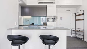 Une cuisine moderne avec des meubles blancs, un îlot central doté de deux tabourets de bar noirs et un four encastré.