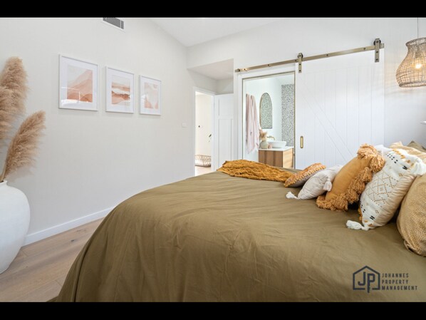 A bedroom with a large bed, a sliding door, a bedside table, and a hanging light fixture.
