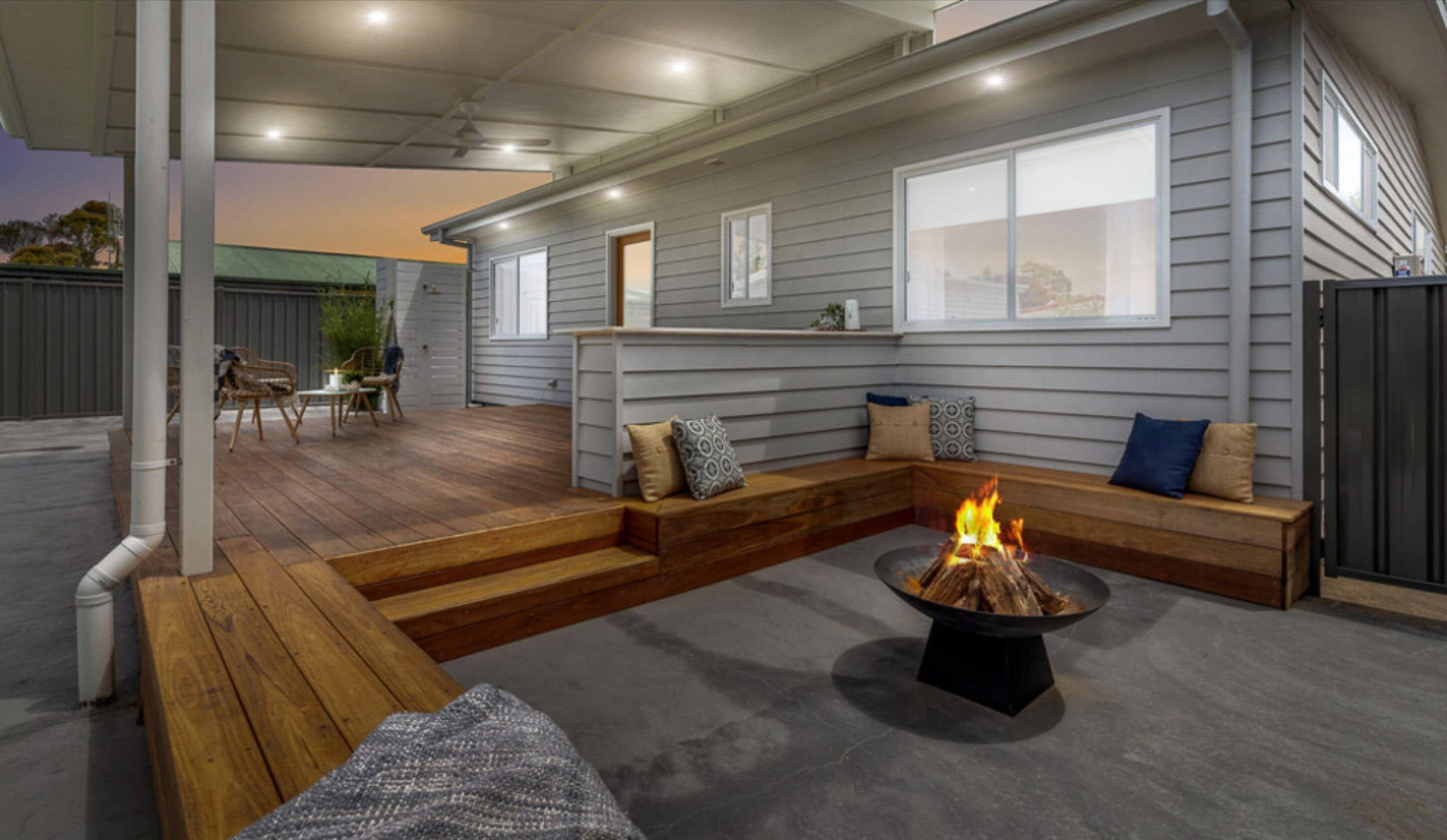 Une terrasse extérieure couverte, dotée d’un foyer, de sièges en bois et offrant une vue sur la maison.
