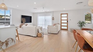 Amplia sala de estar con un sofá grande, otro más pequeño, una mesa de comedor con sillas, y una cocina con mostrador y taburetes.
