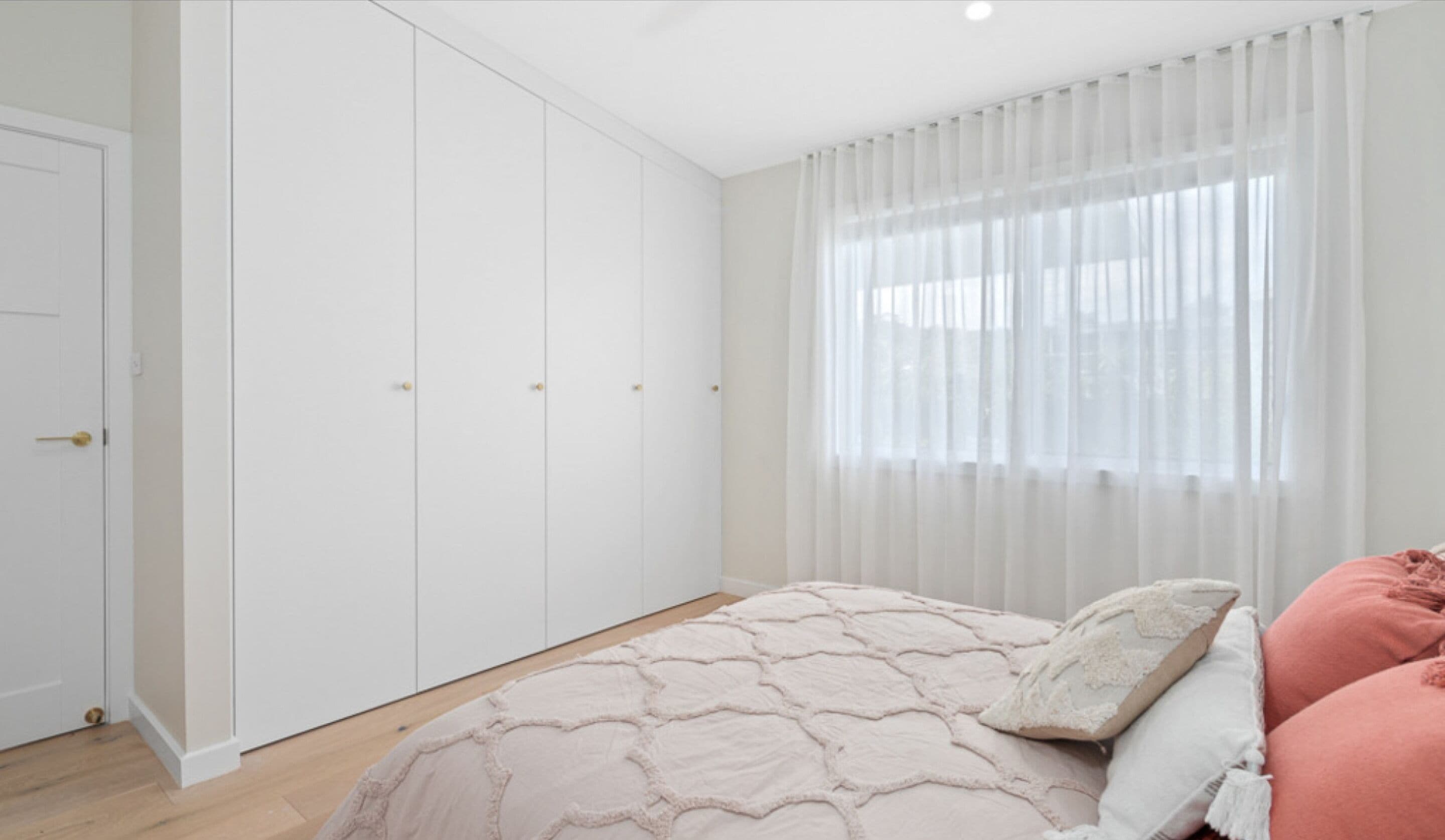 Une chambre à coucher avec un lit, une armoire blanche et une fenêtre ornée de rideaux légers.