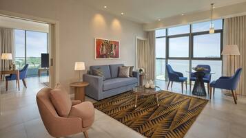 A modern hotel room with a sofa, armchair, dining table, and chairs.