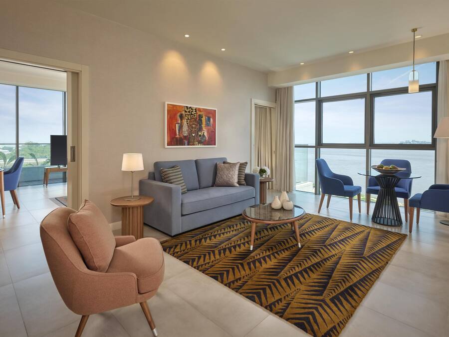 A modern hotel room with a sofa, armchair, dining table, and chairs.