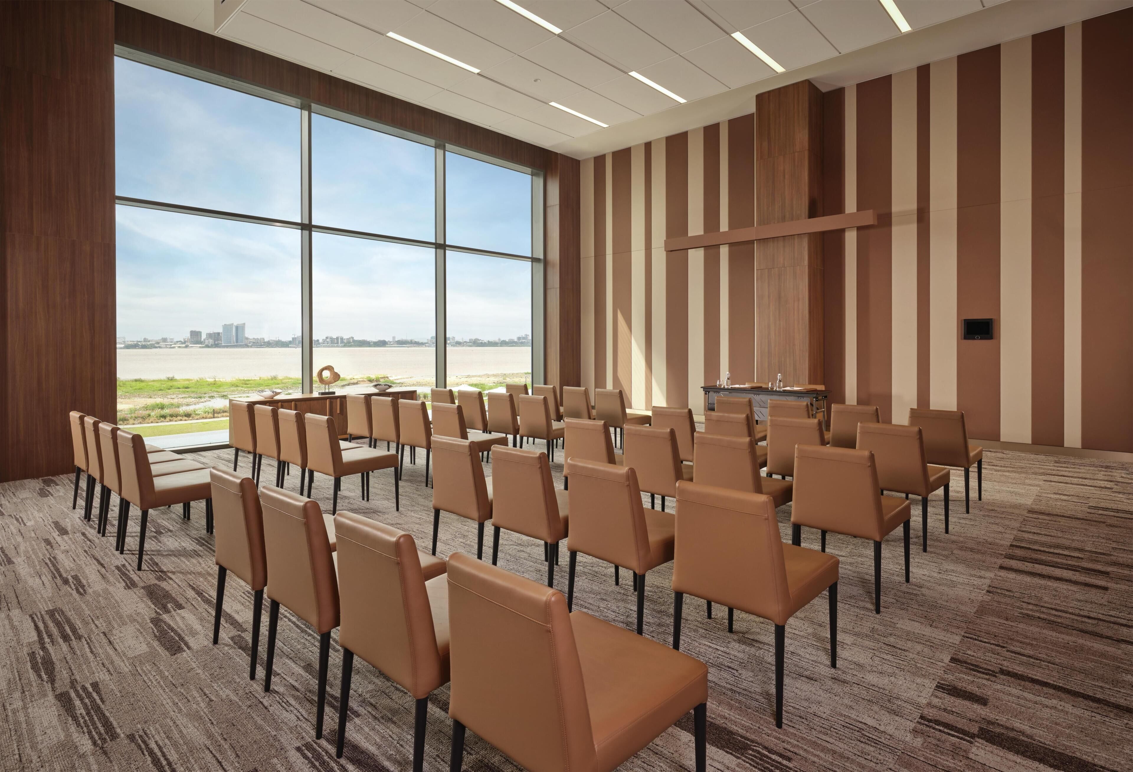 A conference room with a large window, rows of chairs, and a carpeted floor.