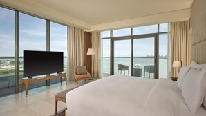 Une chambre d’hôtel avec un grand lit, un téléviseur posé sur un meuble, une chaise, une petite table et une vue sur l’eau.