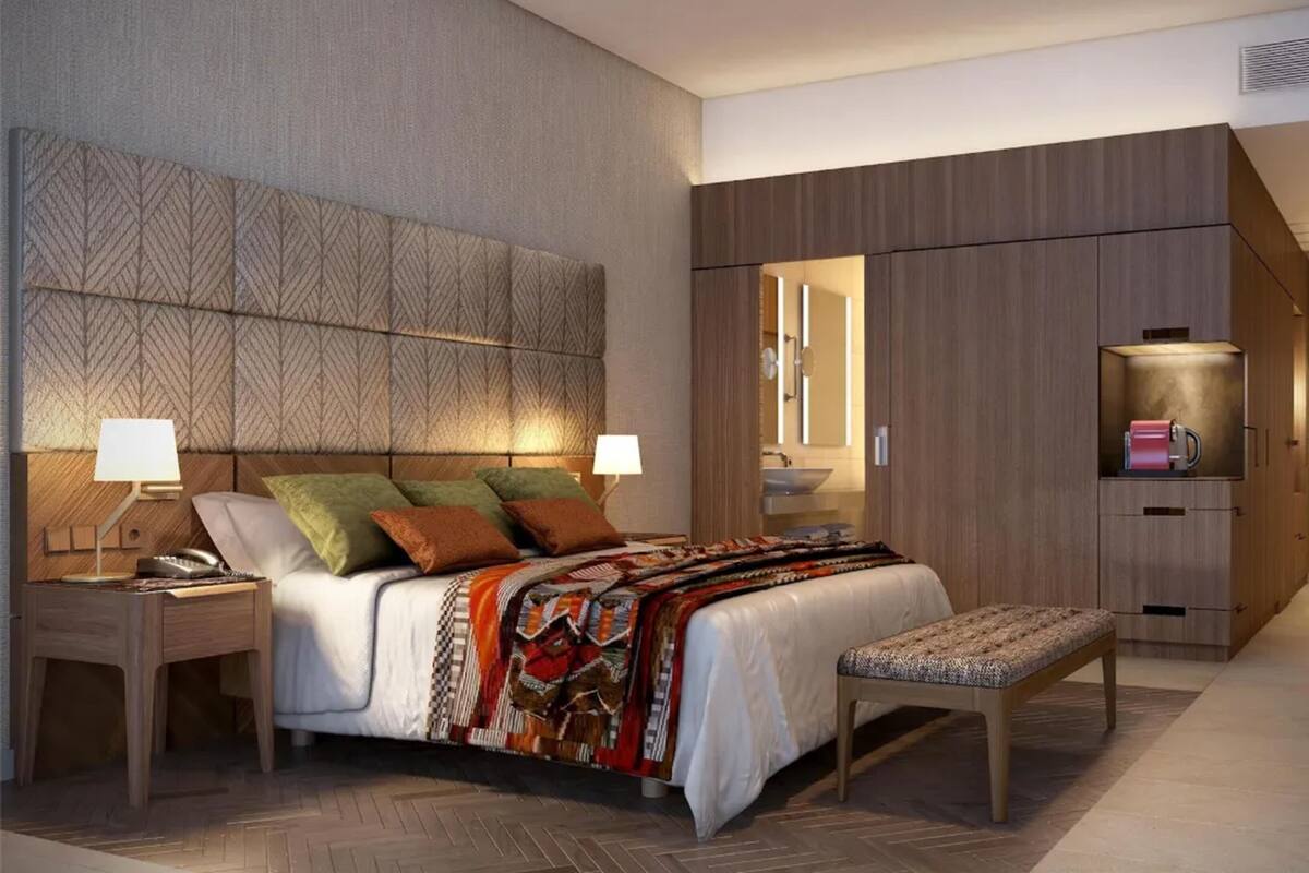 A modern hotel room with a large bed, bedside tables, a bench, a wardrobe, and a mirror.