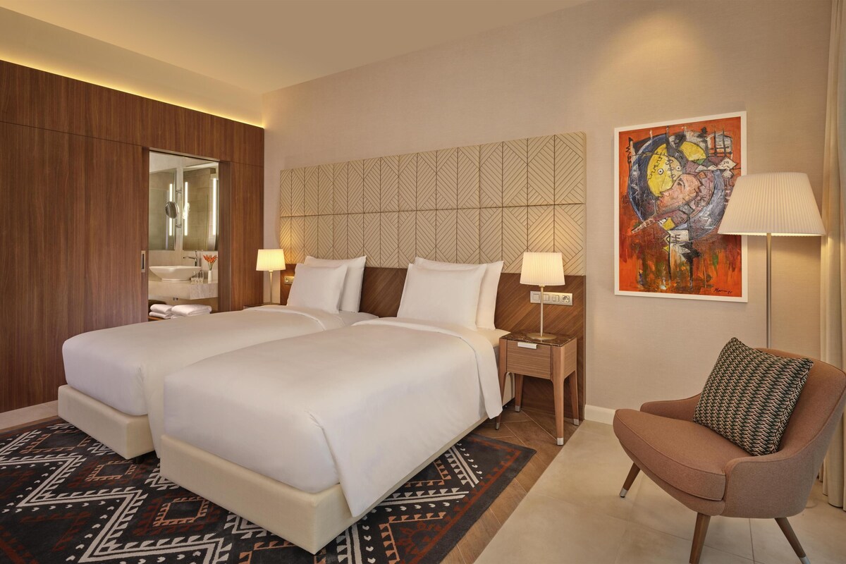 Une chambre d’hôtel avec deux lits, un coin salon, un tableau et un miroir.