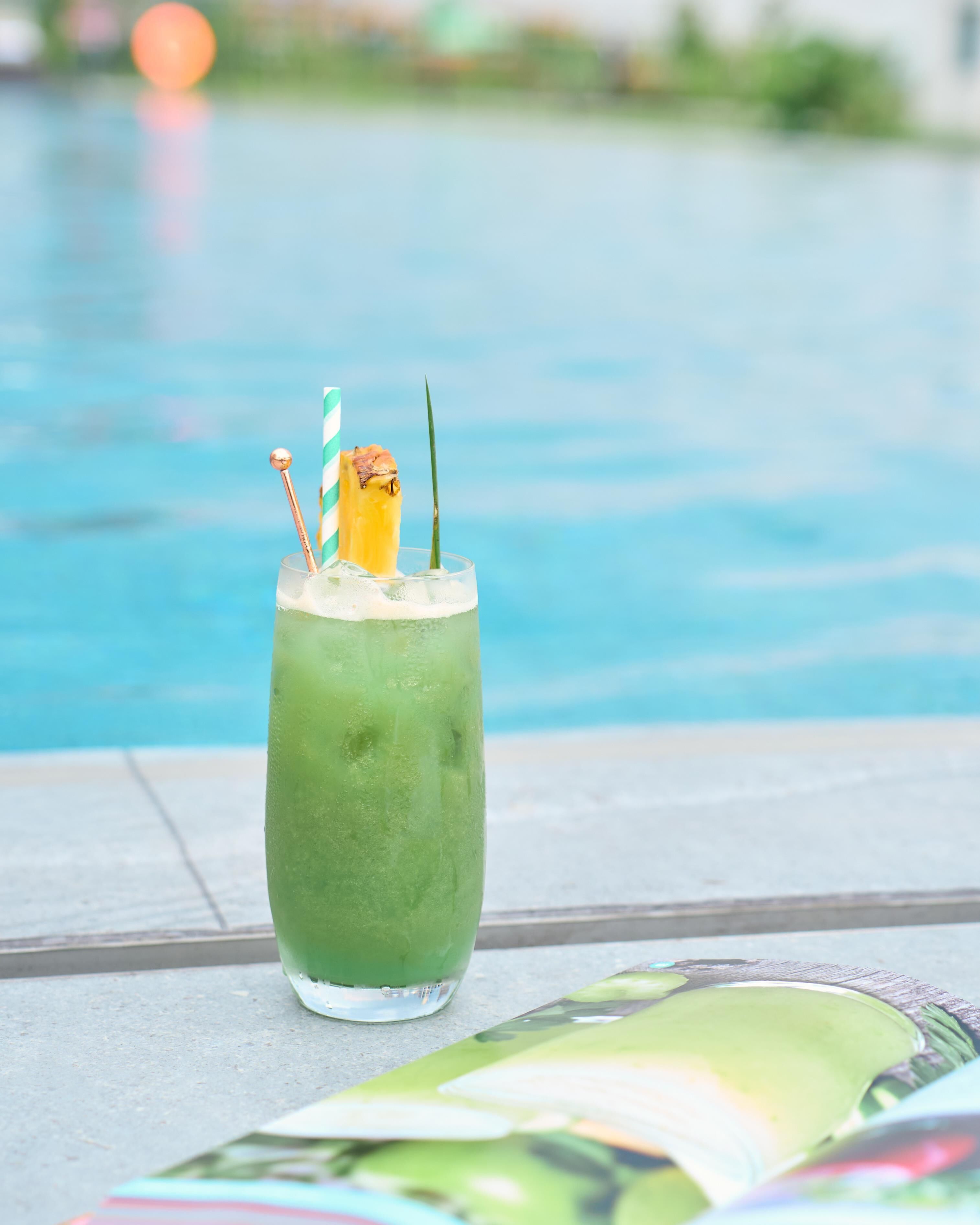 Un cóctel verde con pajita y decoración, sobre una mesa junto a una piscina.