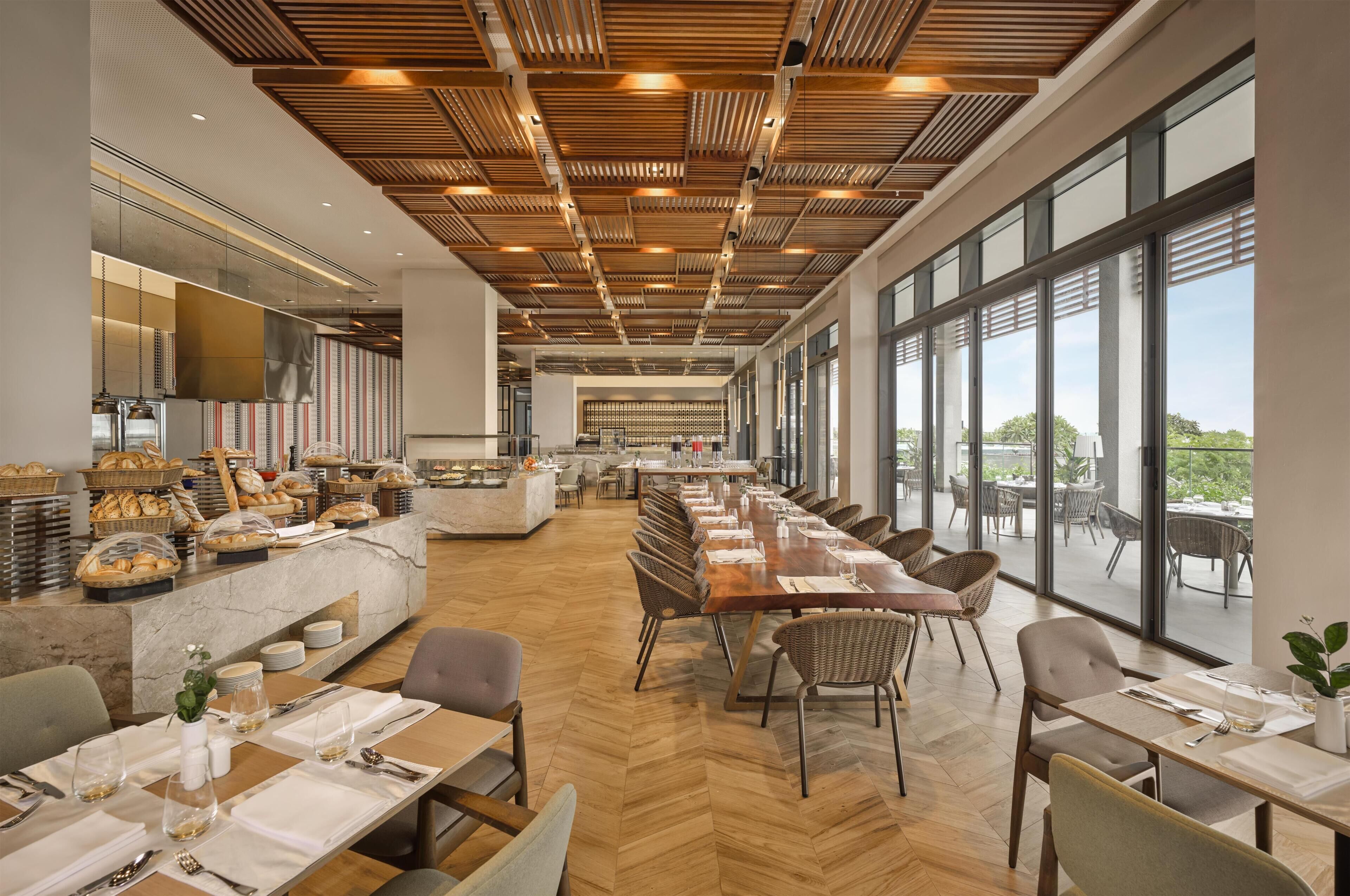 A modern dining area with a long table, chairs, and a buffet with baked goods.