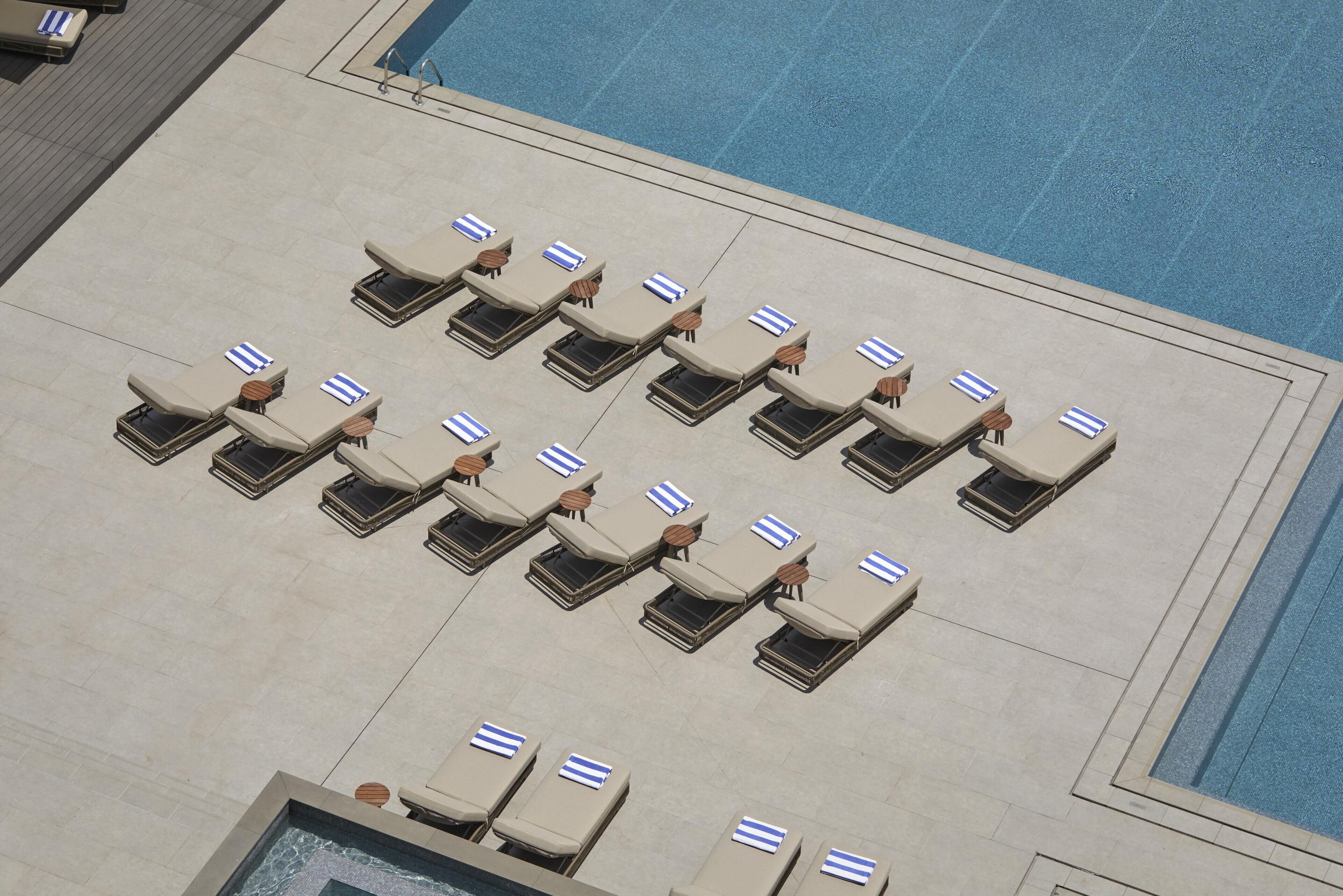 A poolside area with multiple sun loungers arranged in rows, a clear blue pool, and a tiled deck.