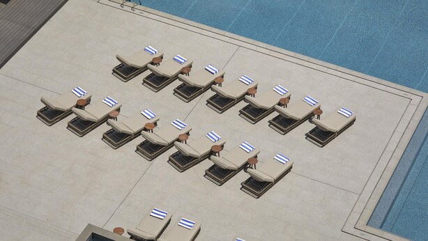 Ein Poolbereich mit mehreren Liegestühlen, die in Reihen angeordnet sind, einem klaren, blauen Pool und einer gefliesten Terrasse.