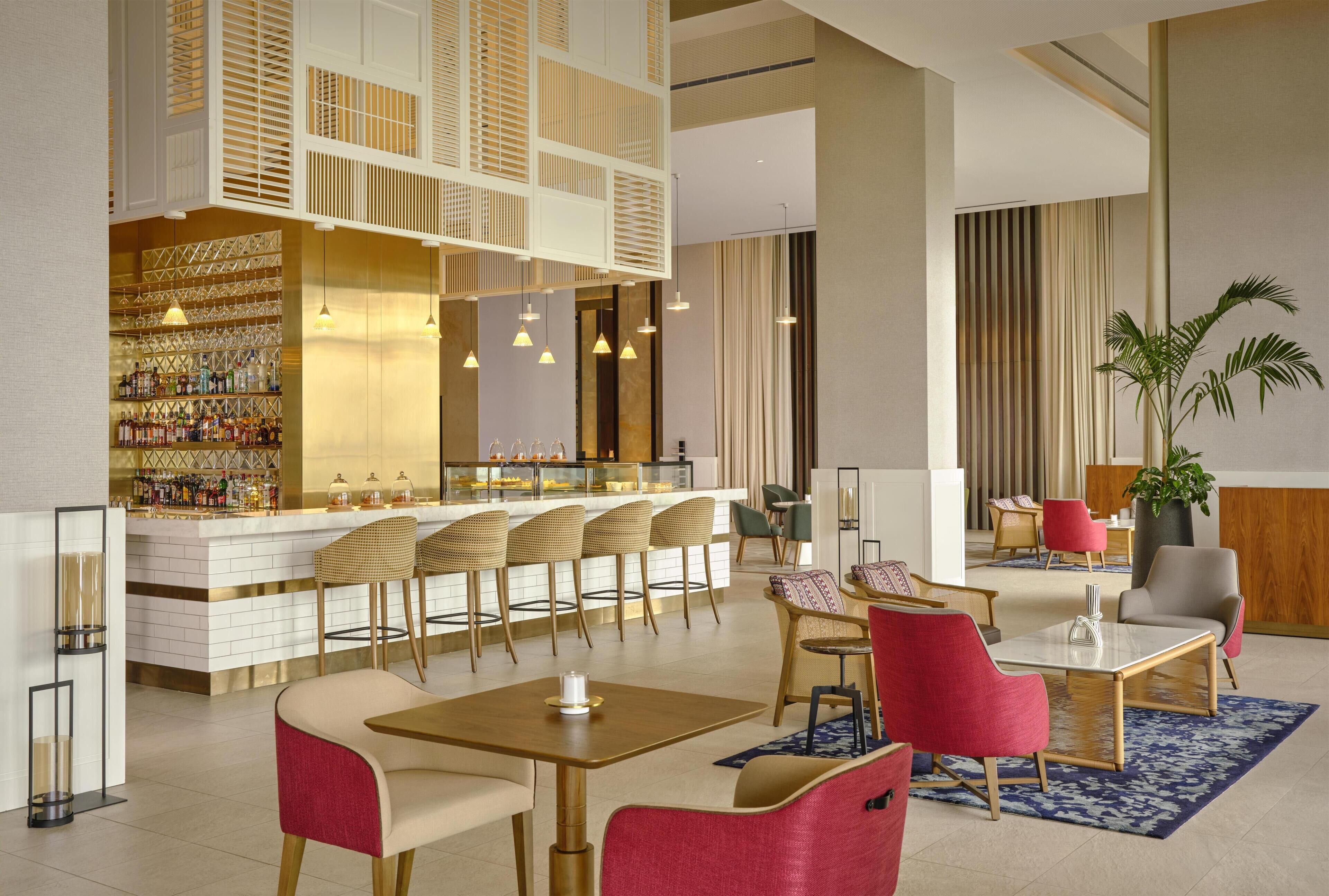 Un área de bar moderna con mostrador, varias opciones de asientos, incluyendo taburetes y sillas, y una planta grande en maceta.