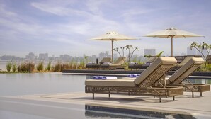Une piscine sur le toit, agrémentée de chaises longues et de parasols, avec une vue sur les toits de la ville en arrière-plan et un ciel dégagé.